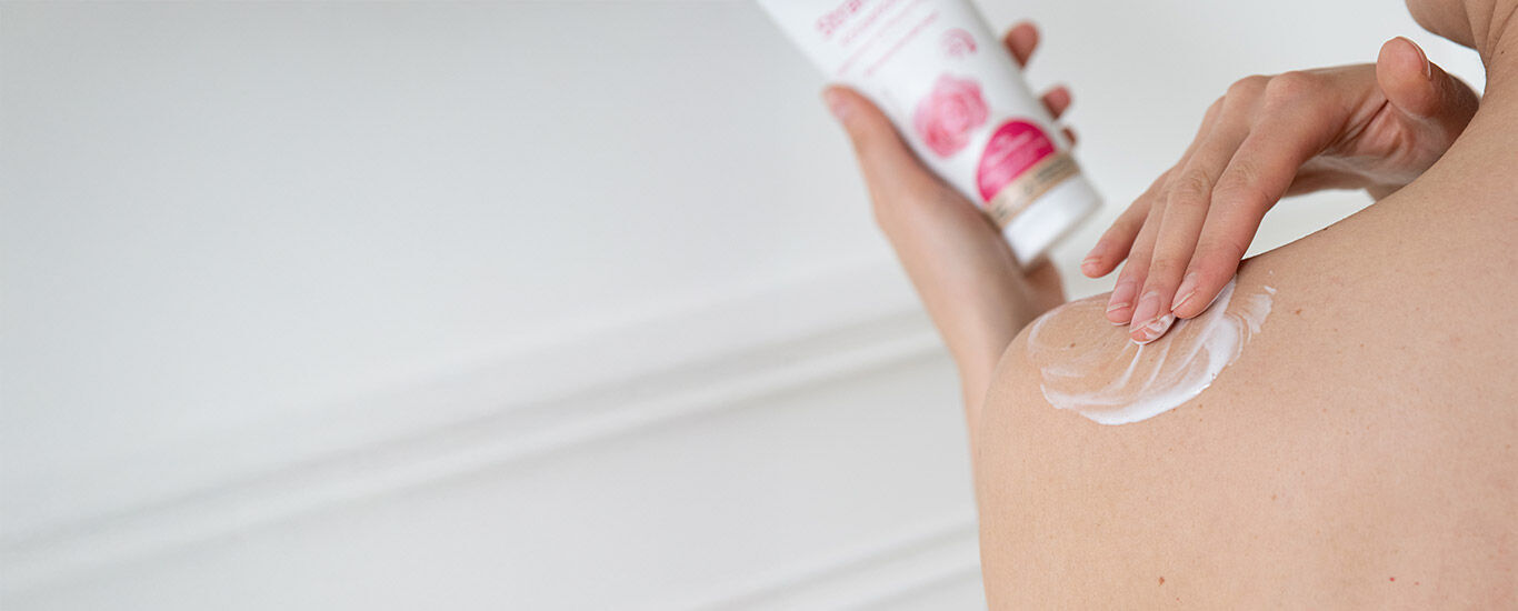 Schouder van een vrouw van achteren. Vrouw brengt schoudercrème aan, Kneipp bodylotion op de achtergrond. 